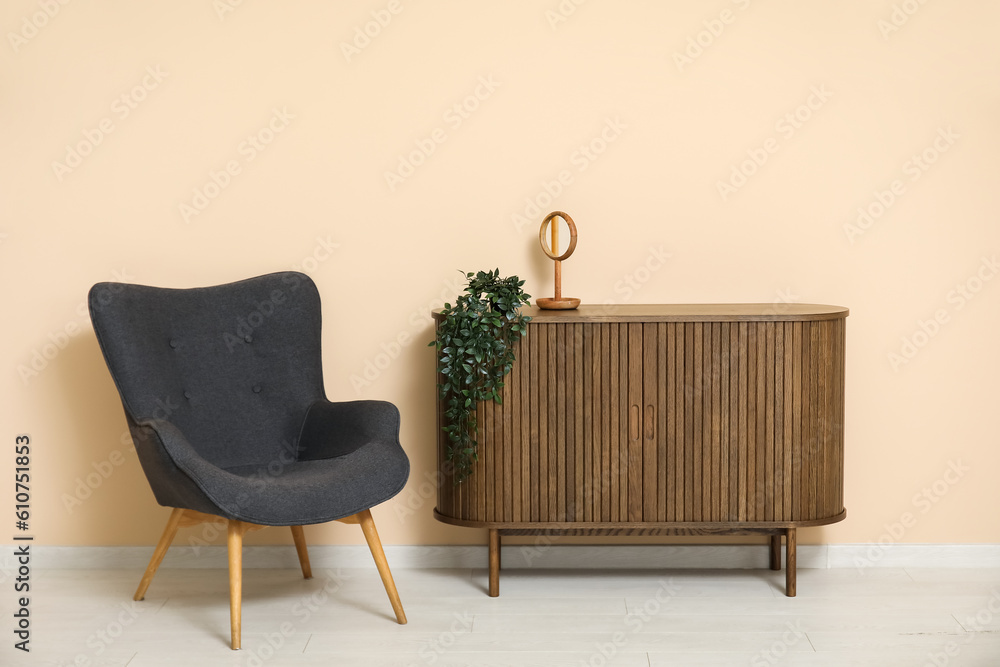 Dark grey armchair with dresser, mirror and houseplant near beige wall