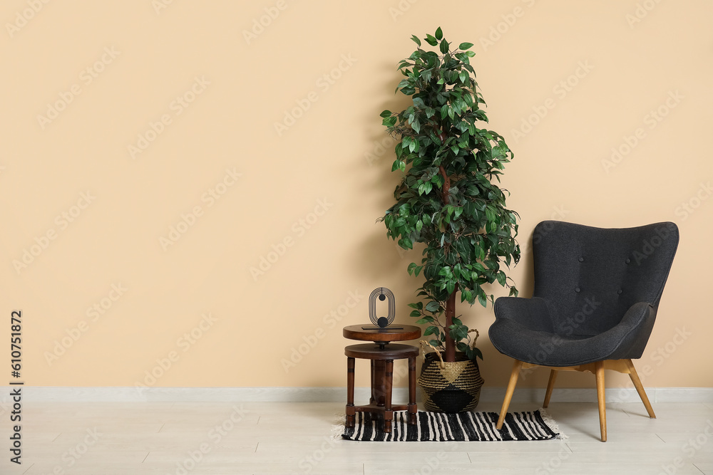 Dark grey armchair with small coffee table, houseplant and rug near beige wall