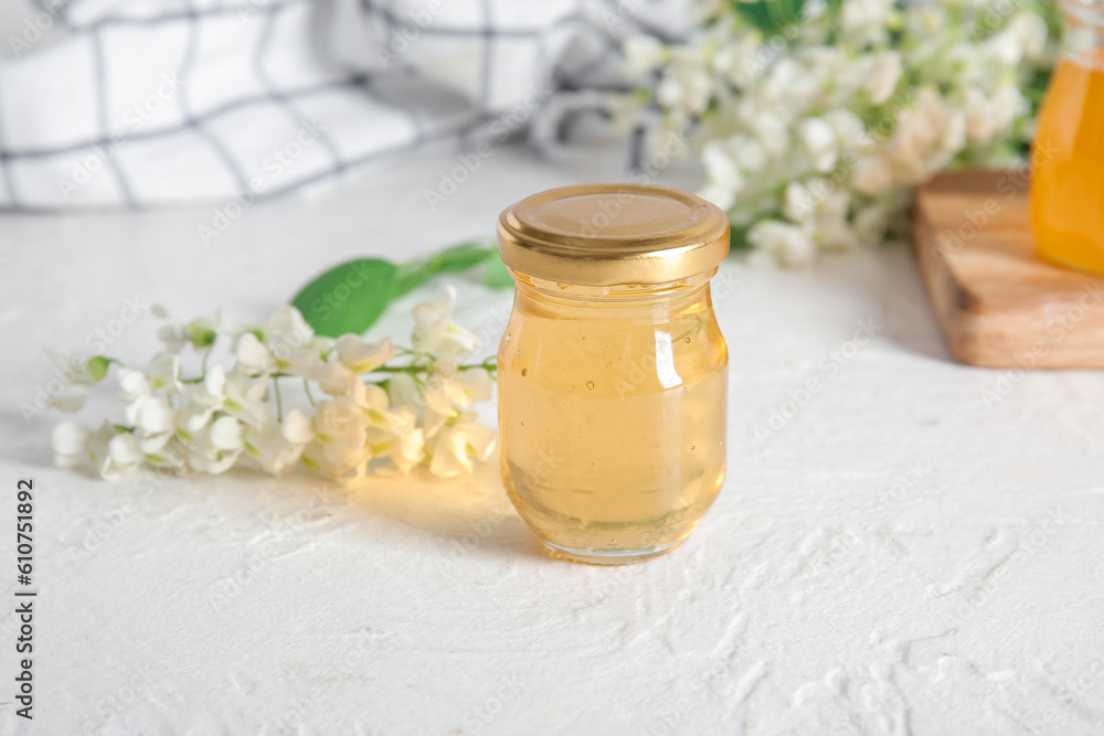 Jar of honey with flowers of acacia on light background, closeup