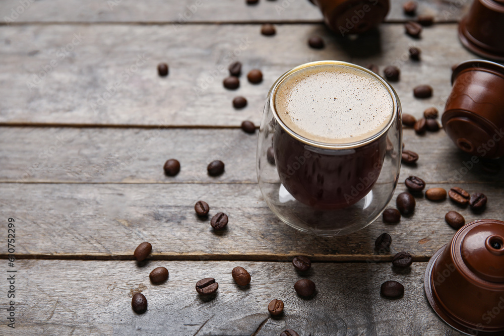 Glass of delicious coffee, pods and beans on wooden table