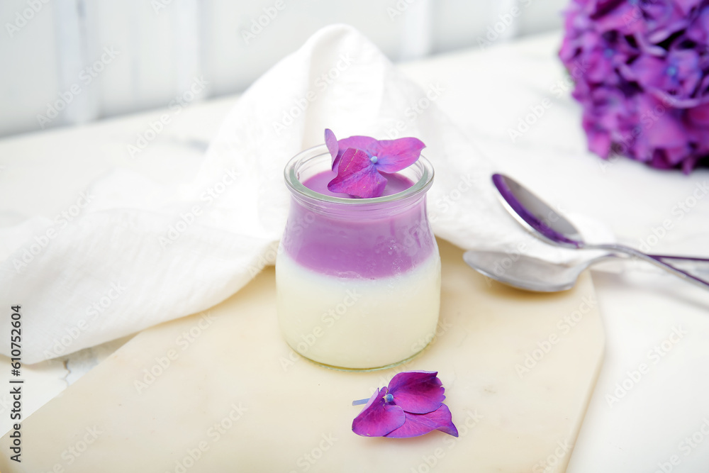 Glass of panna cotta with beautiful hydrangea flowers on white table