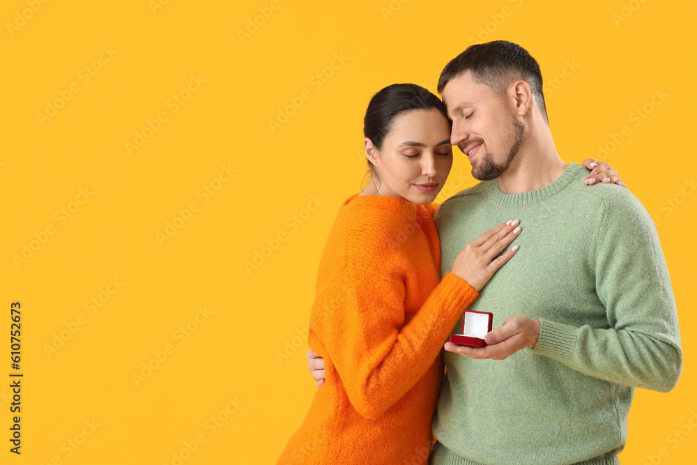 Young man proposing to his girlfriend on yellow background