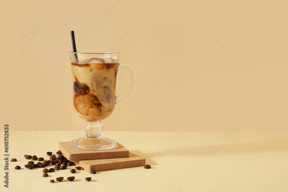 Glass of ice coffee with straw and beans on yellow table near beige wall