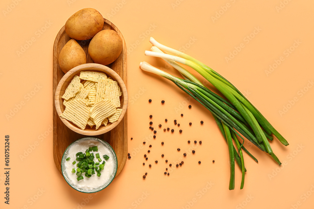 Bowl of tasty sour cream with sliced green onion and potato chips on orange background