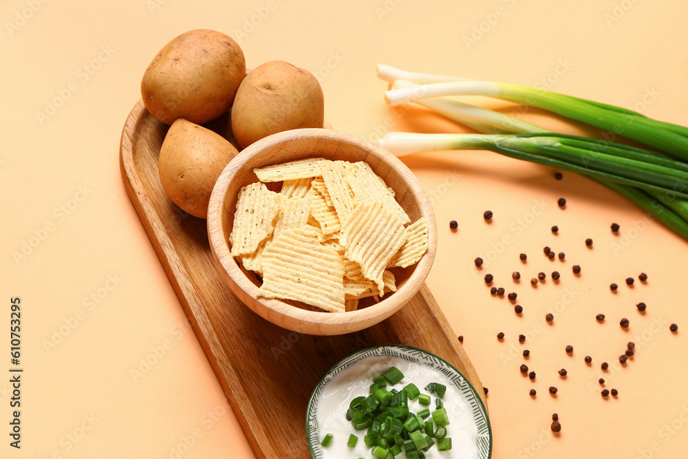 Bowl of tasty sour cream with sliced green onion and potato chips on orange background