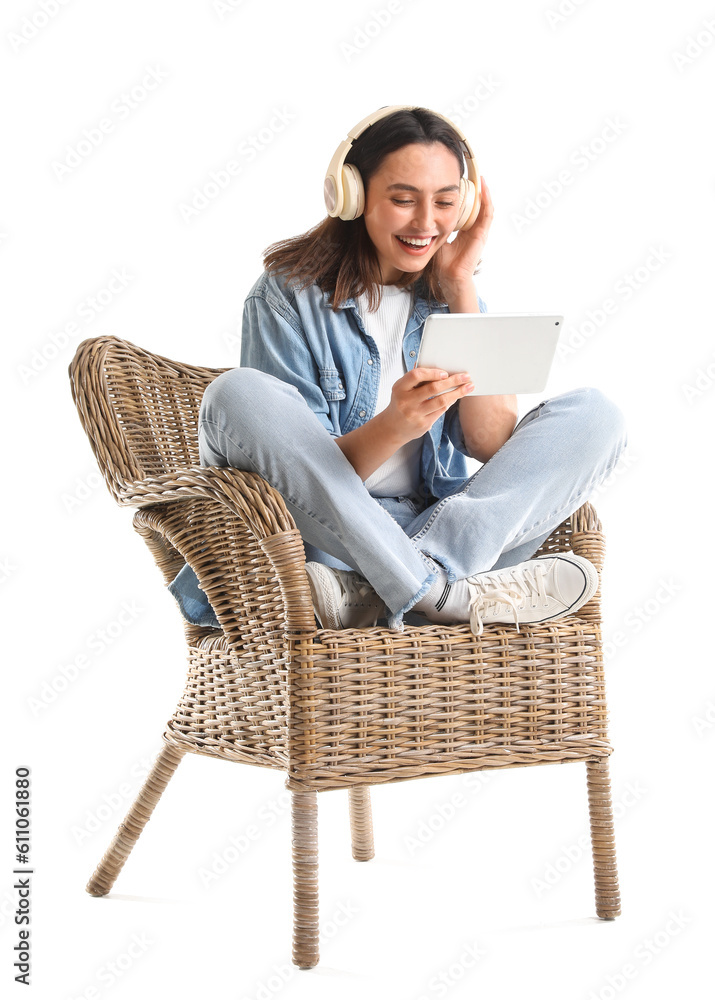 Young woman with headphones using tablet computer in wicker armchair on white background