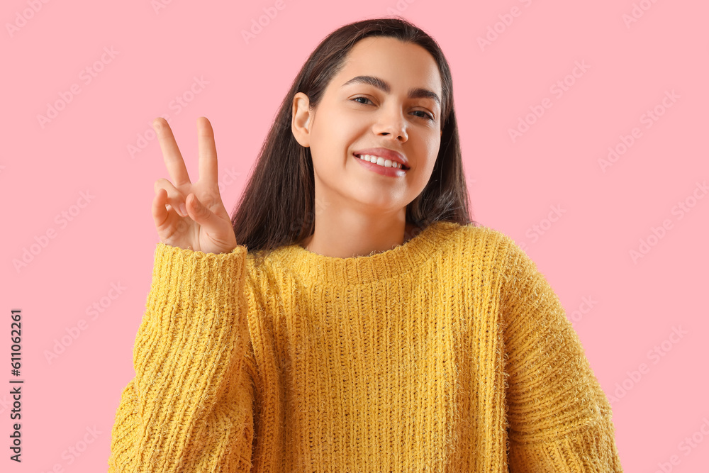 Beautiful young woman showing victory gesture on pink background, closeup