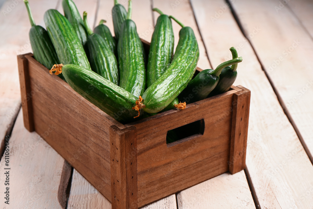 Box with fresh cucumbers on light wooden background