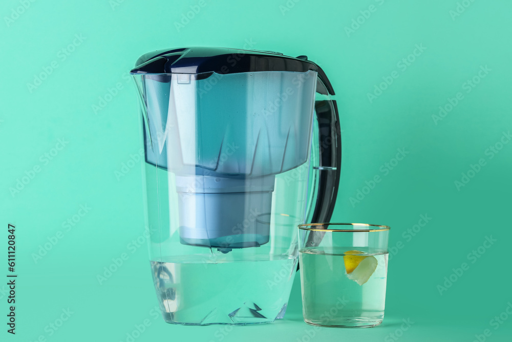 Water filter jug and glass with citrus slice on green background