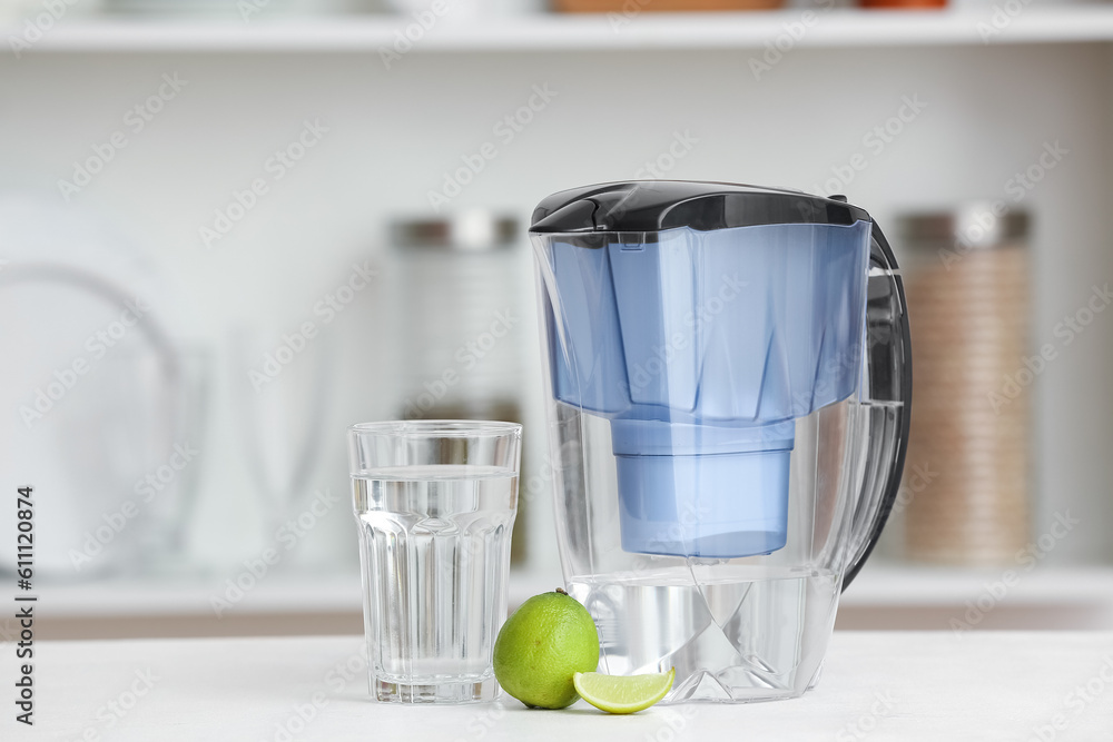 Water filter jug with glass and lime on table in kitchen