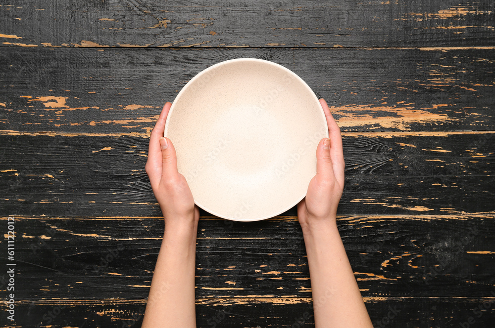 Female hands with empty plate on black wooden background