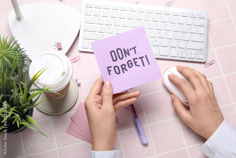 Woman with dont forget reminder using computer on pink tile background