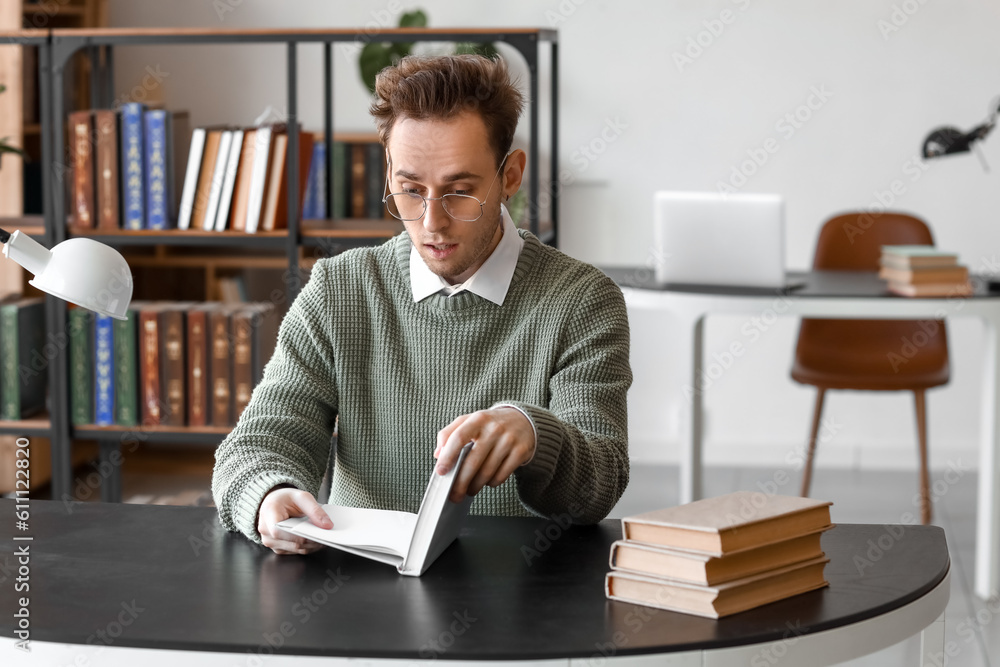 Shocked young man reading book at table in library