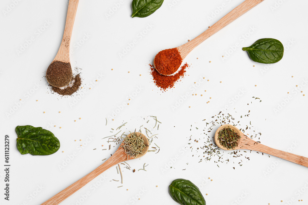 Composition with wooden spoons of aromatic spices and spinach leaves on light background