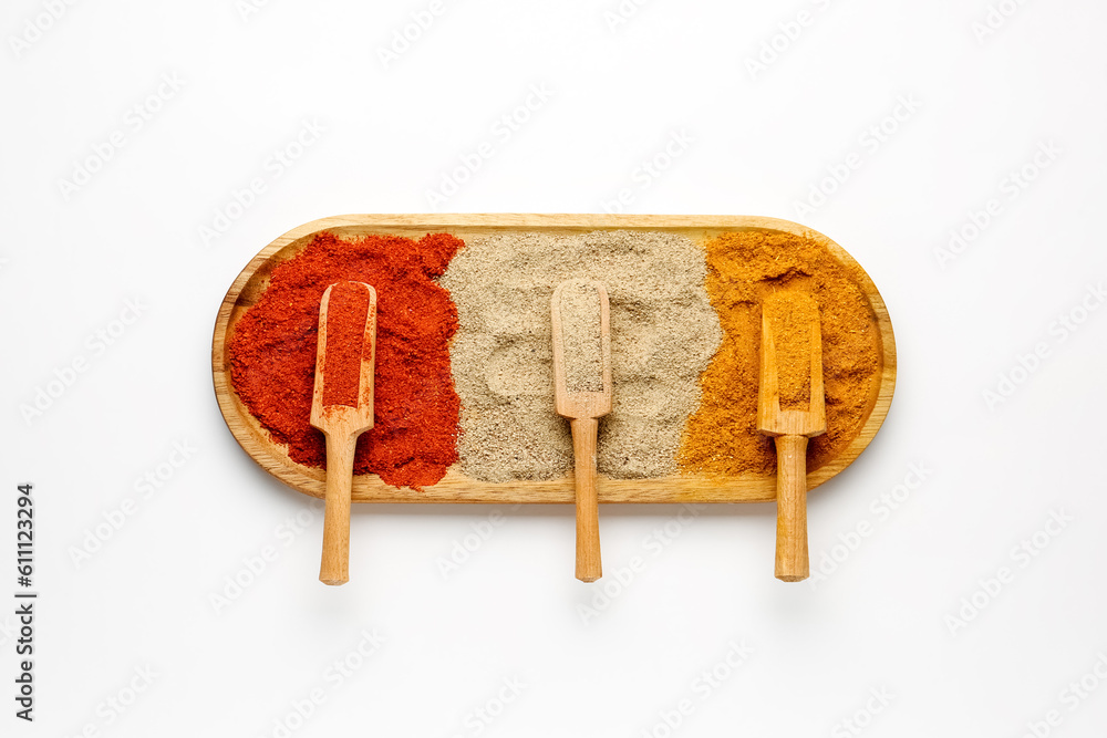 Wooden board with scoops of aromatic spices on light background