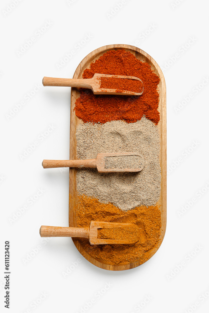 Wooden board with scoops of aromatic spices on light background