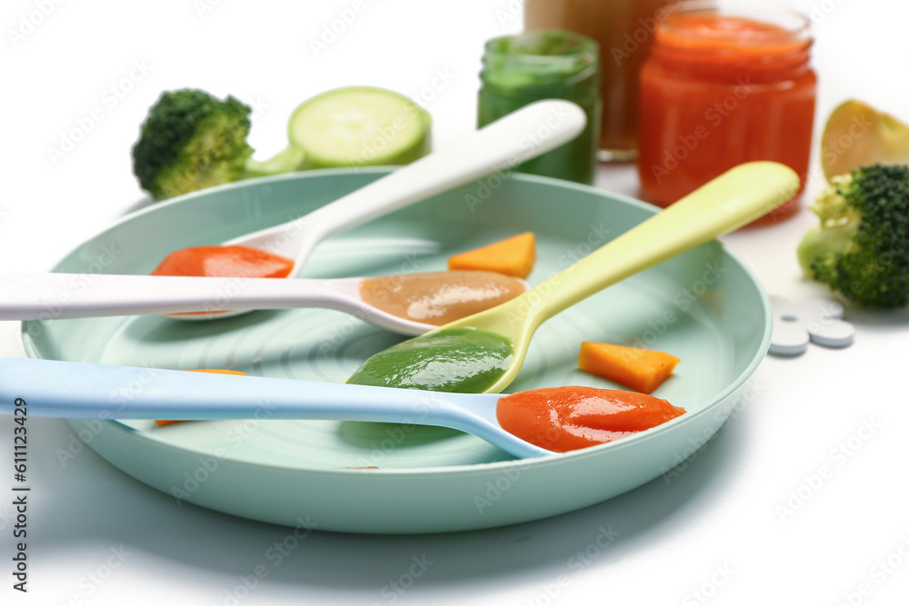 Plate with spoons of healthy baby food on white background, closeup