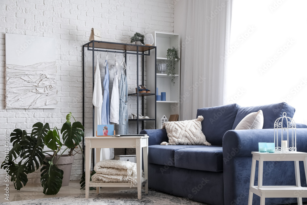 Interior of light room with sofa, shelving unit and clothes