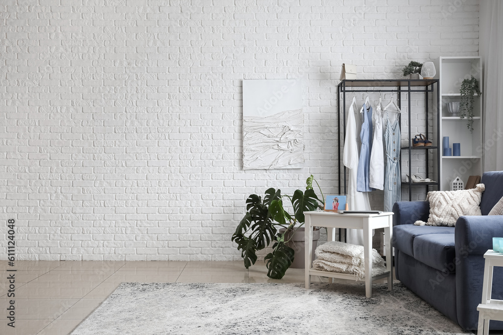 Interior of light room with sofa, shelving unit and clothes