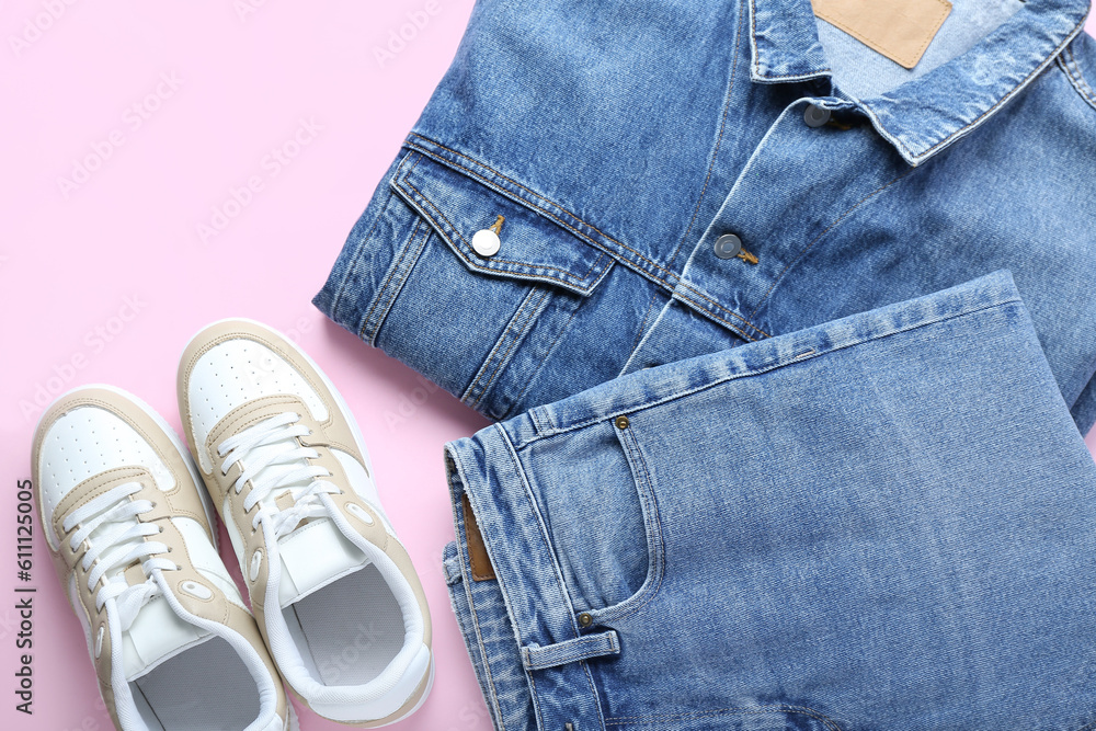 Stylish jeans with denim jacket and sneakers on pink background