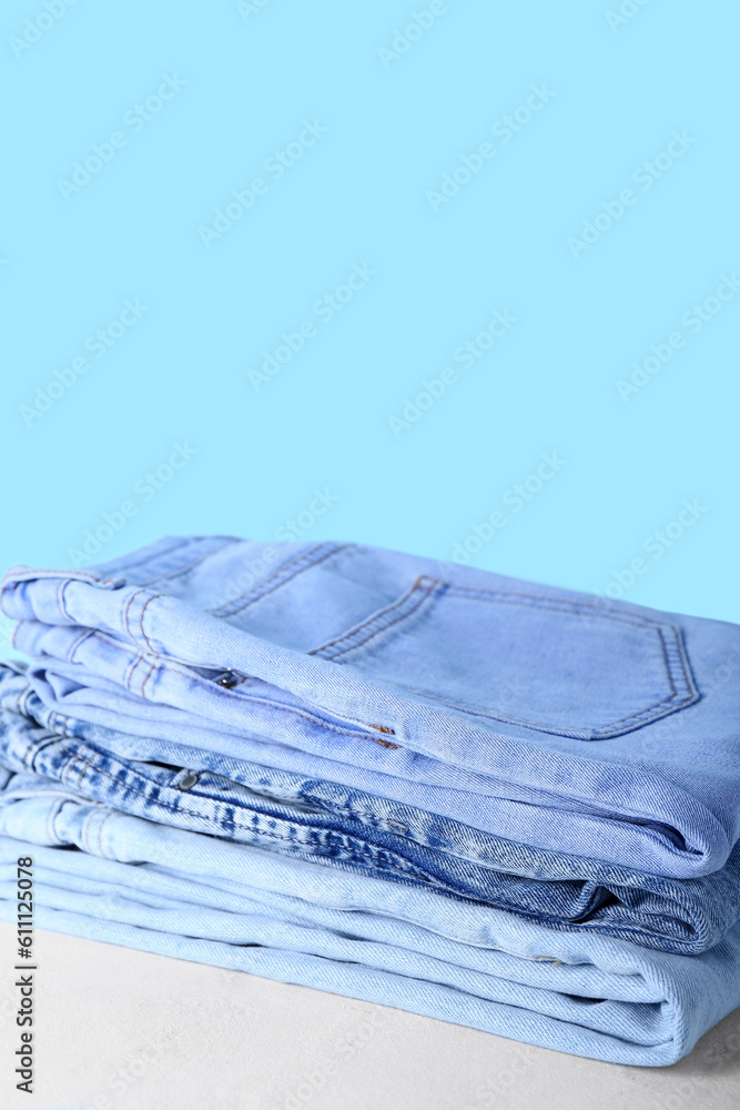 Stack of jeans on table near blue wall, closeup