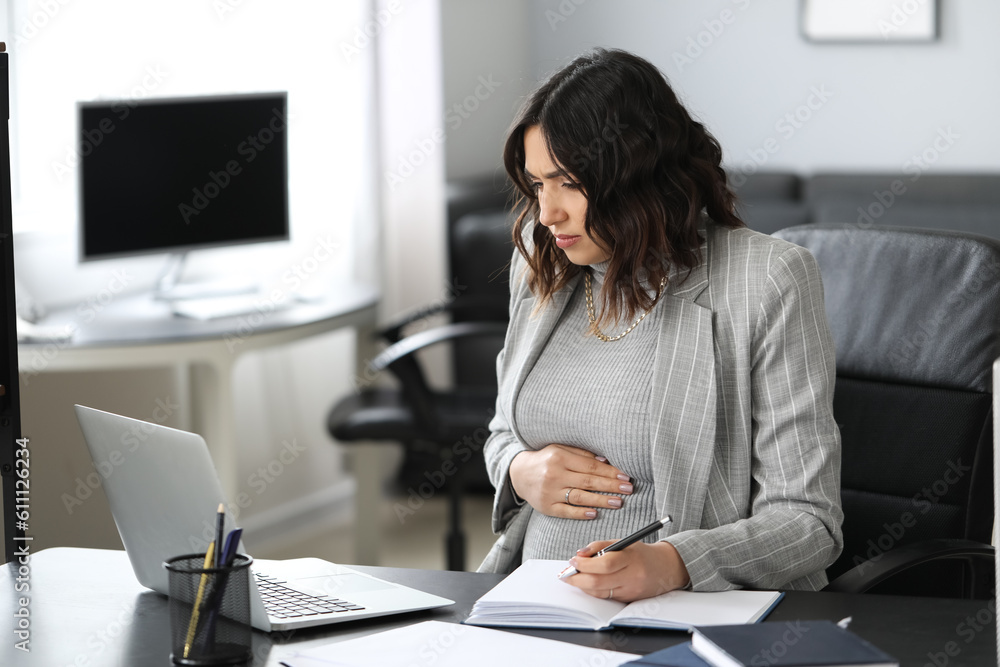 Young pregnant woman working at table in office