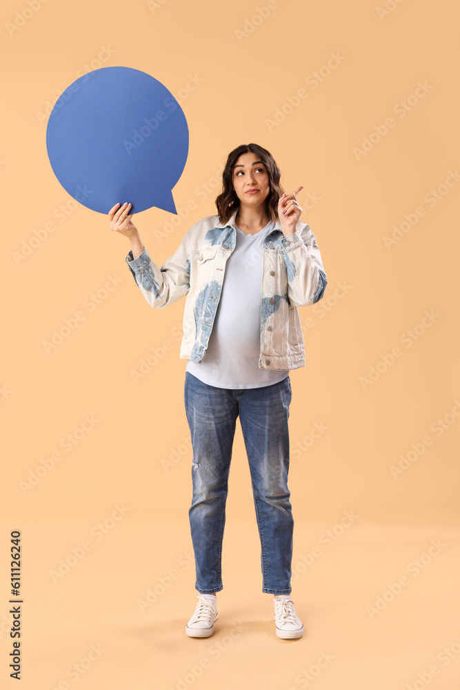 Young pregnant woman with blank speech bubble pointing at something on beige background