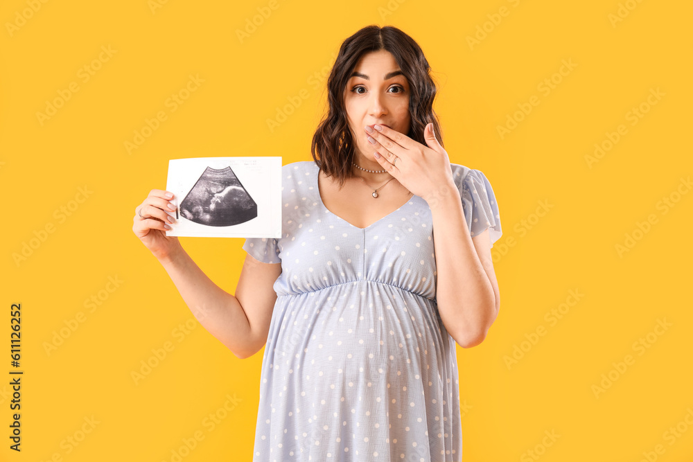 Surprised young pregnant woman with sonogram image on yellow background