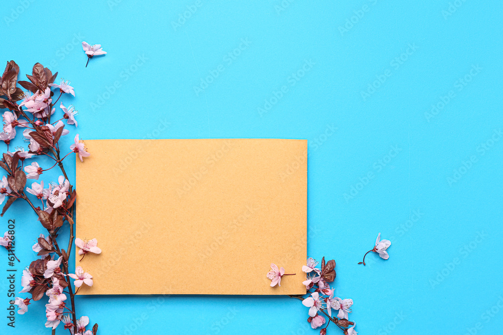 Blooming tree branches with pink flowers and blank greeting card on blue background