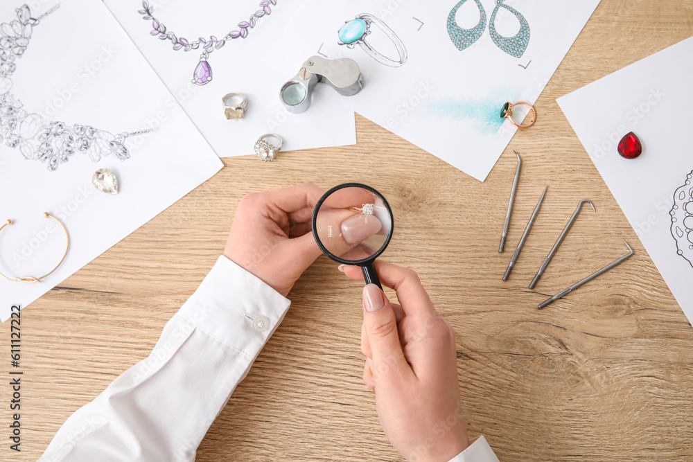 Female jeweler examining ring on wooden table, top view