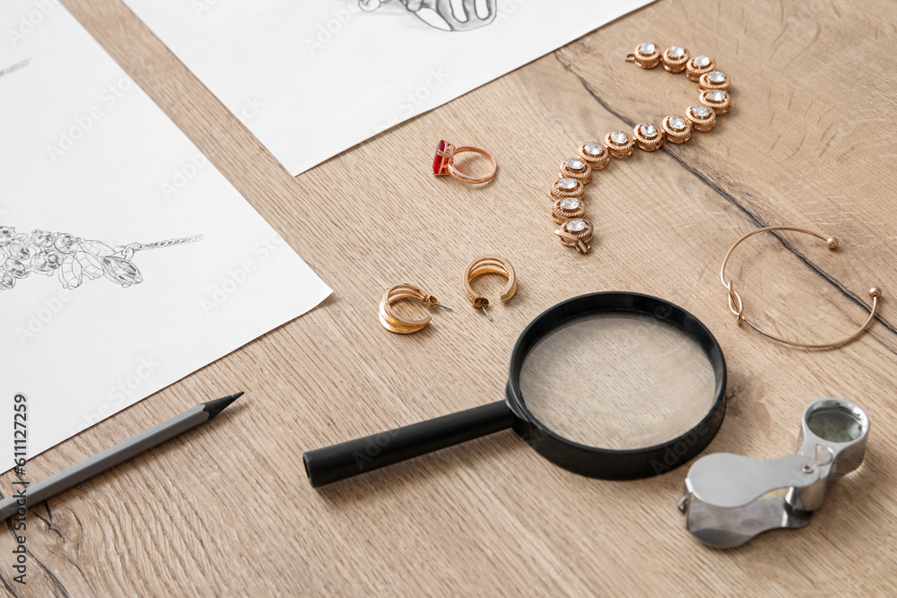 Jewelers magnifiers with accessories and drawings on wooden table, closeup