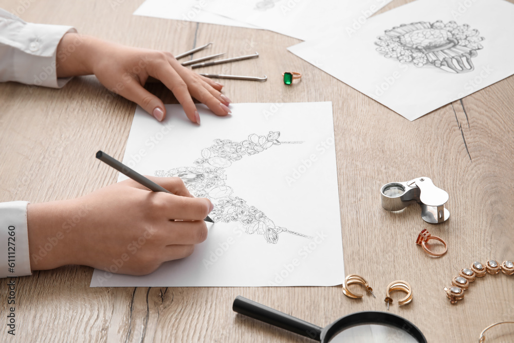 Female jeweler drawing adornment on wooden table, closeup