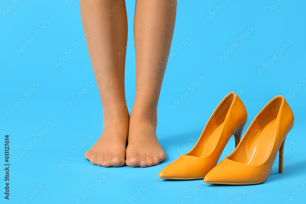 Female legs in tights with stylish high heels on color background, closeup