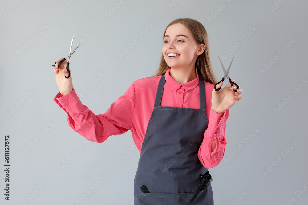 Female hairdresser with scissors on grey background