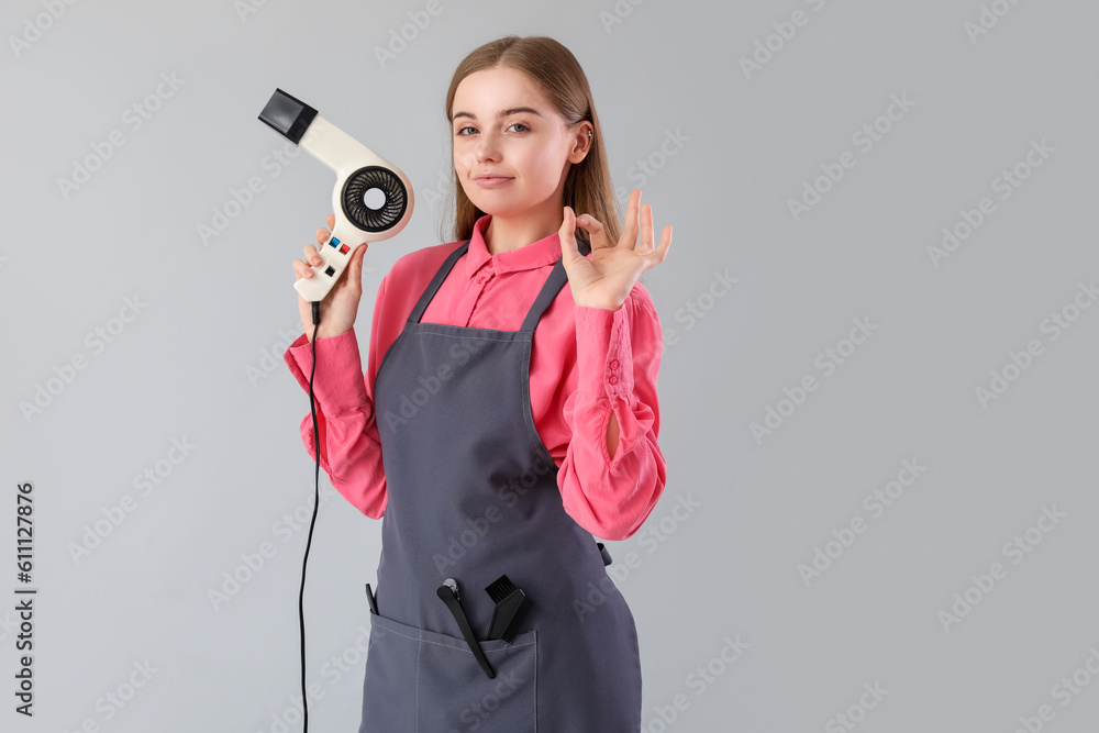 Female hairdresser with dryer showing OK on grey background