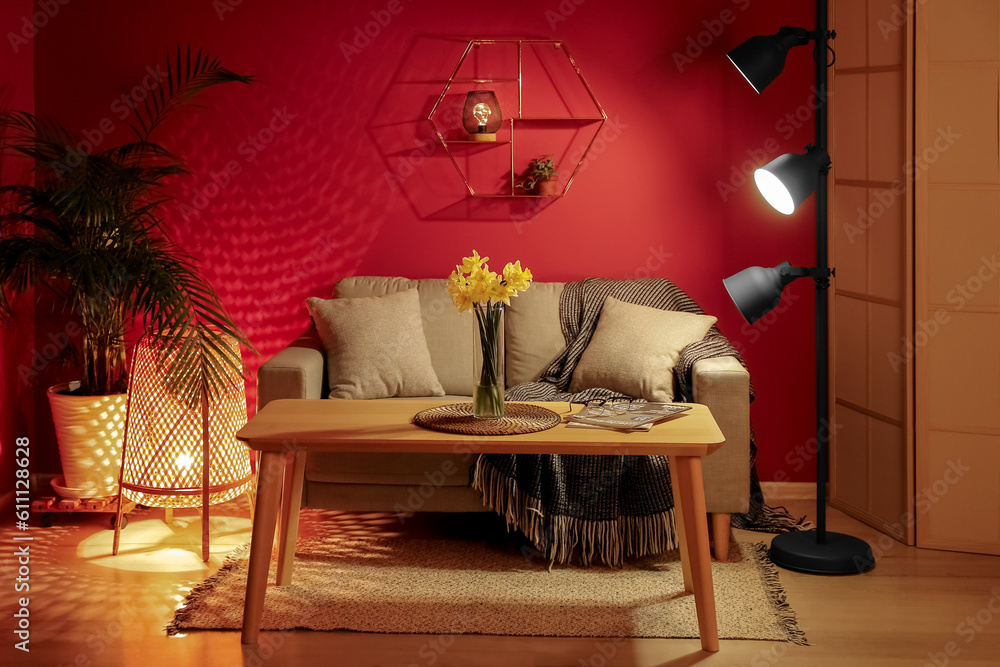 Interior of cozy living room with grey sofa and narcissus flowers on table at night