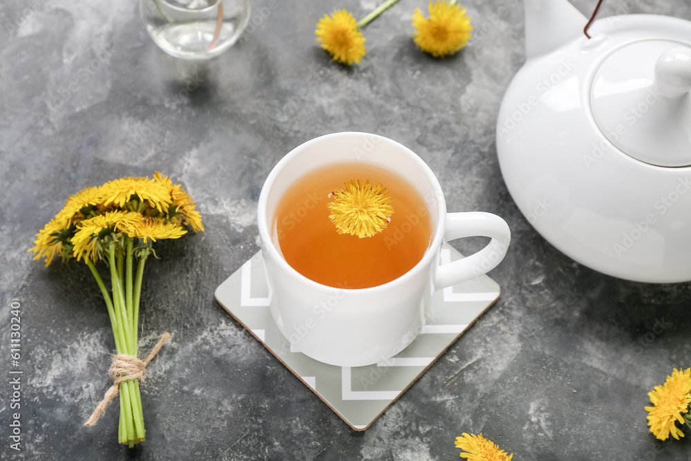 Cup of healthy dandelion tea and teapot on grey background