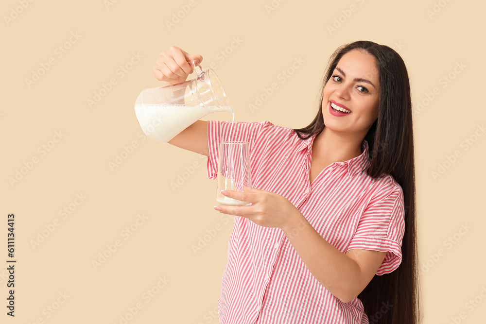 Beautiful young woman pouring milk into glass on beige background