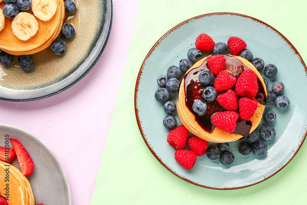 Plates with sweet pancakes and berries on color background