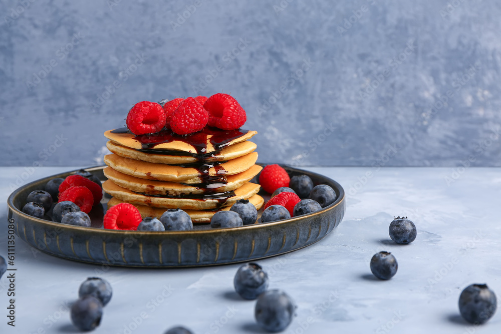 Plate with tasty pancakes and berries on blue background, closeup