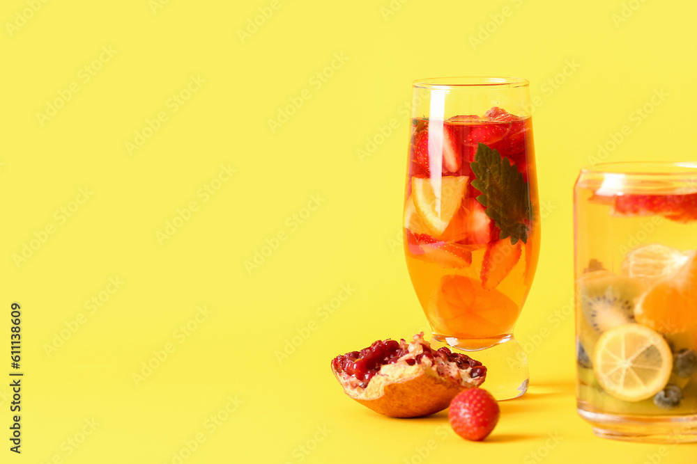 Glasses of infused water with different sliced fruits on yellow background