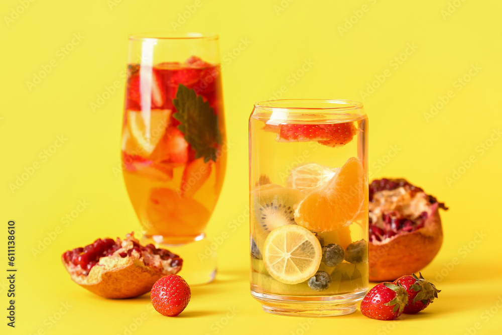 Glasses of infused water with different sliced fruits on yellow background