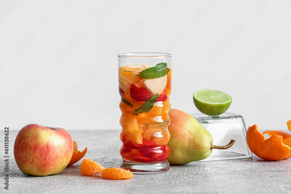 Glass of infused water with different sliced fruits on grey table