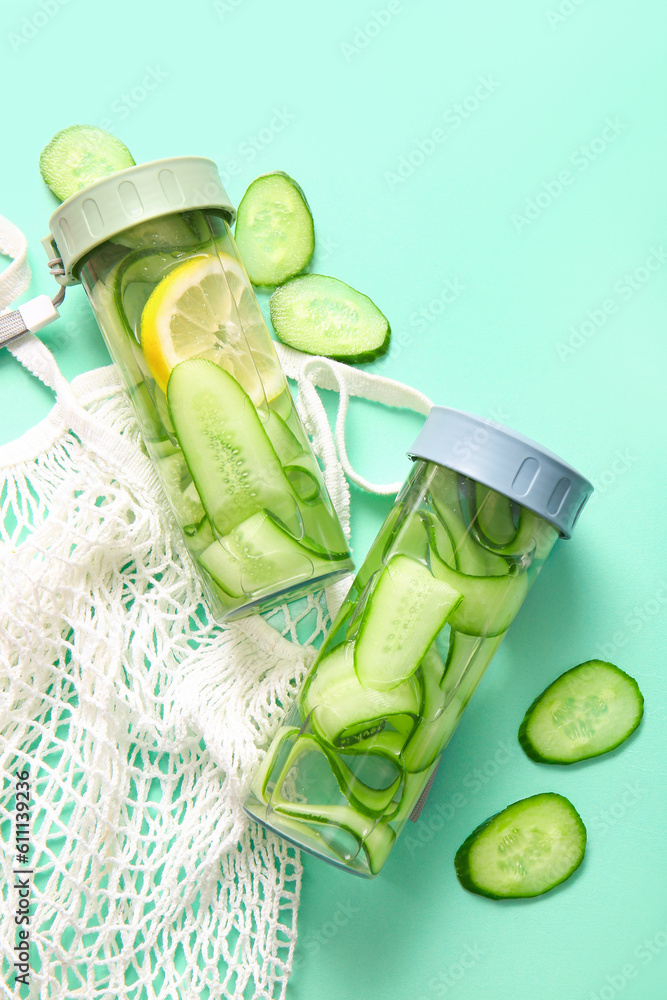 Sports bottles of infused water with cucumber slices on turquoise background