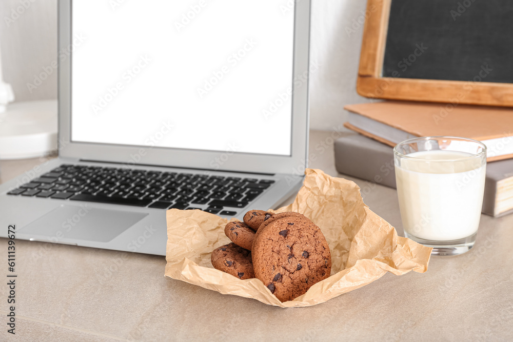 Cookies with glass of milk and laptop on table in room