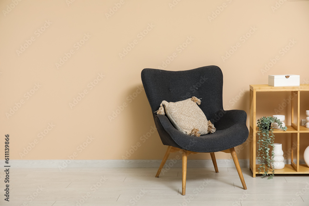 Dark grey armchair with pillow, shelving unit and houseplants near beige wall