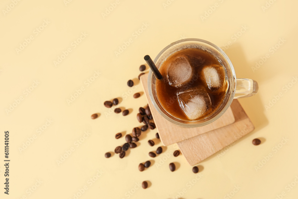 Glass of ice coffee with straw, beans and wooden boards on yellow background