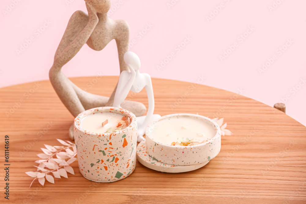 Holders with candles and decor on table near pink wall in room