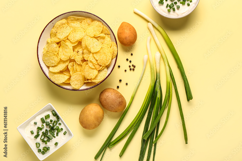 Bowl of tasty sour cream with sliced green onion and potato chips on yellow background