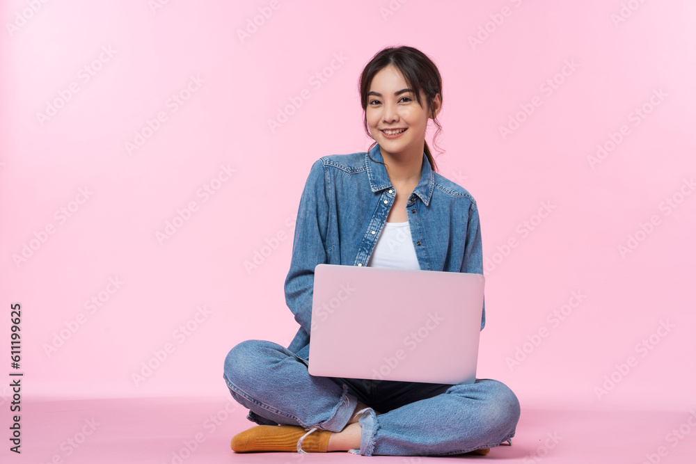 Young Asian college student sits cross-legged on floor working with a laptop computer, looking direc